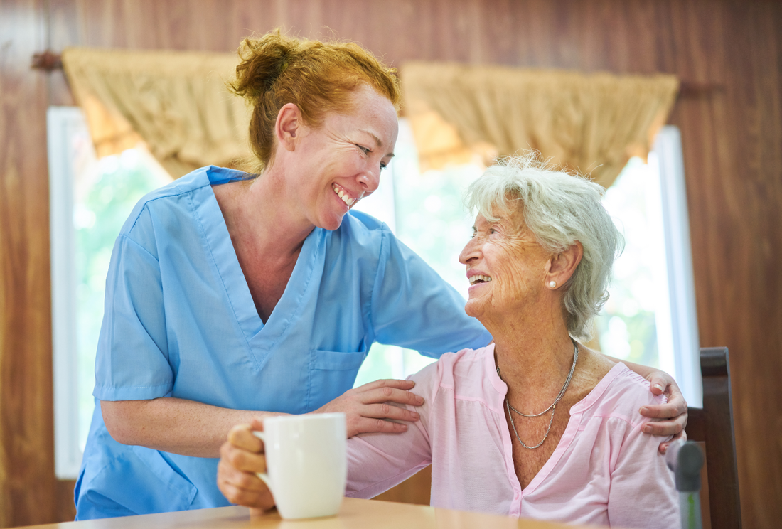 Red headed home care worker and her elderly client smile at each other.