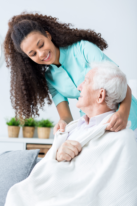 Home care worker standing behind an elderly man with a broken arm sitting down.